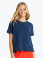 A smiling blonde woman wearing a navy blue short-sleeve crewneck t-shirt and bright red shorts, photographed against a clean white background.