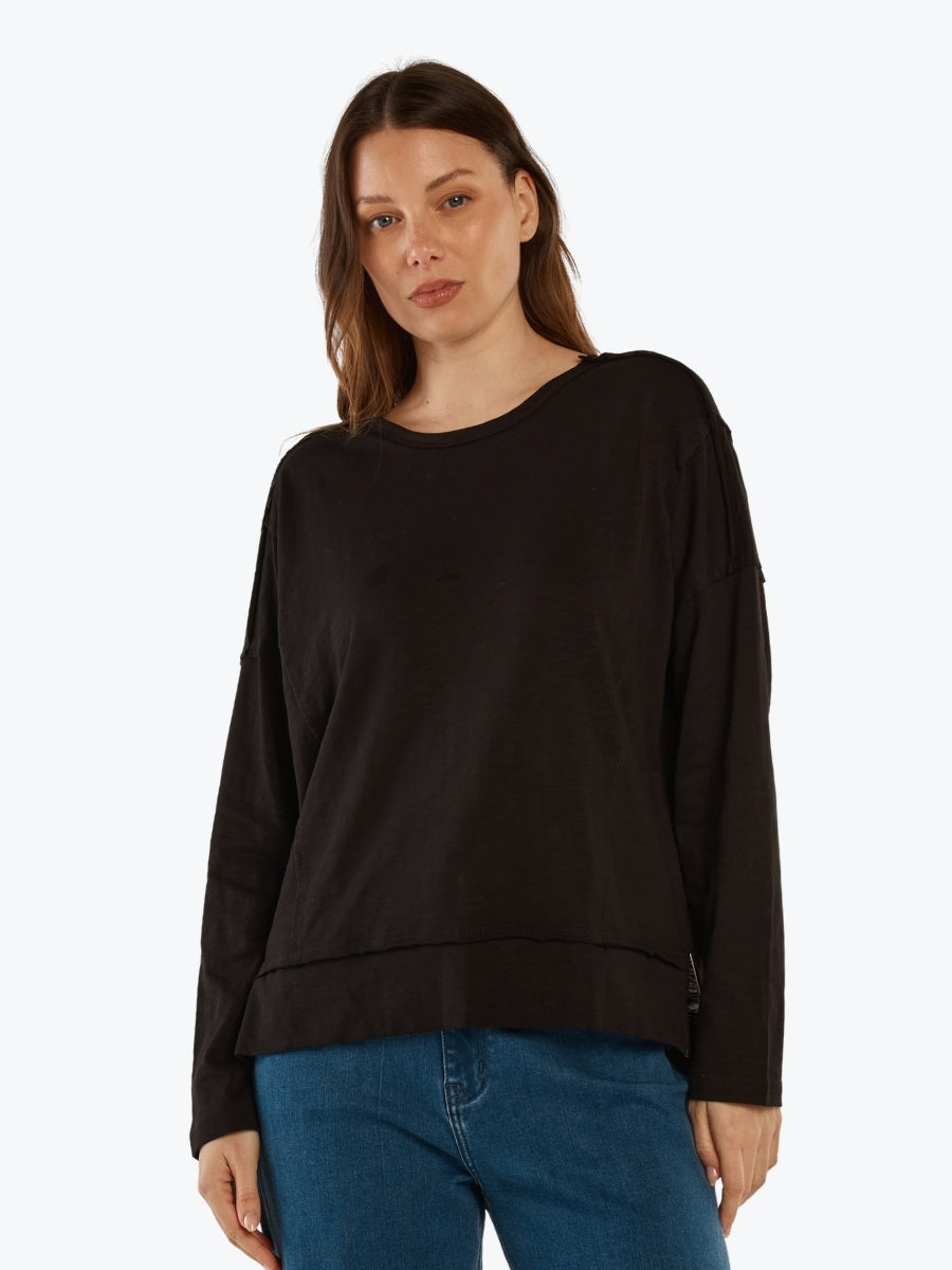 Woman wearing a black long-sleeve top and blue jeans on a white background