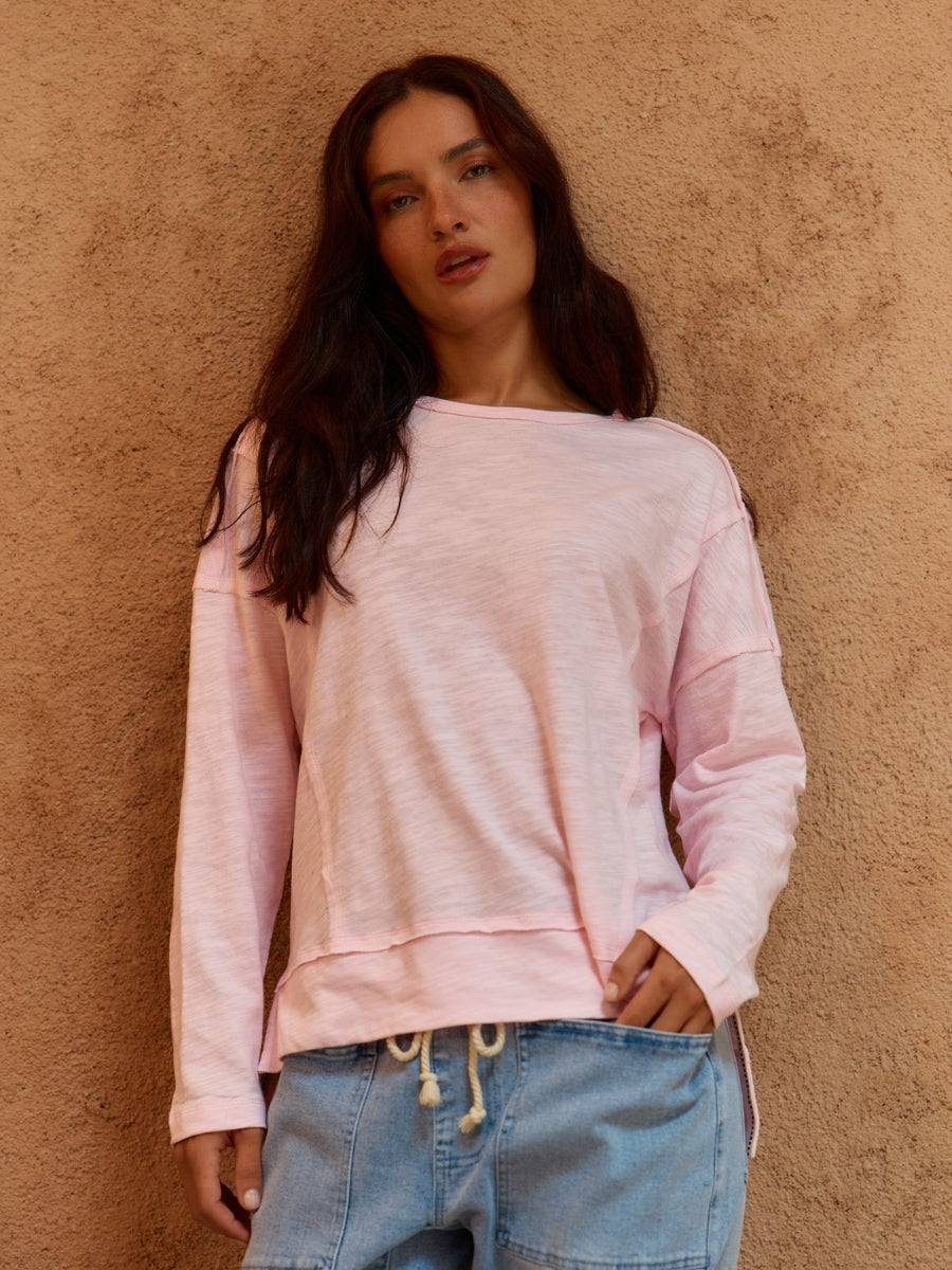 Woman wearing a pink sweatshirt and blue jeans against a beige wall