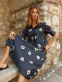 Woman wearing a black  dress with beige  print sitting against a stone wall.