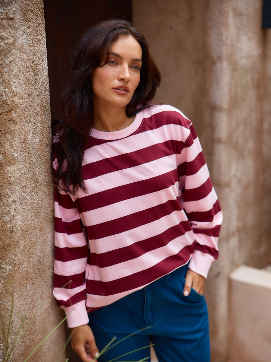 Woman wearing a red and white striped sweater and blue pants, leaning against a stone wall.