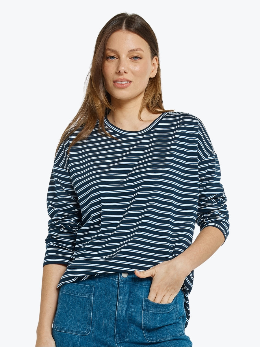Woman wearing a blue and white striped shirt with blue jeans on a light gray background