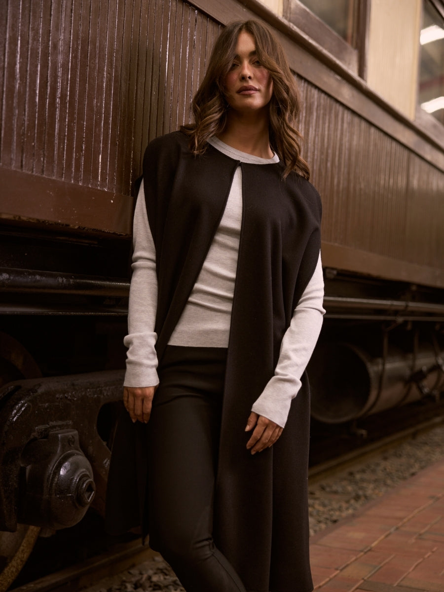 Woman in a black vest and white long-sleeve shirt standing next to a train.