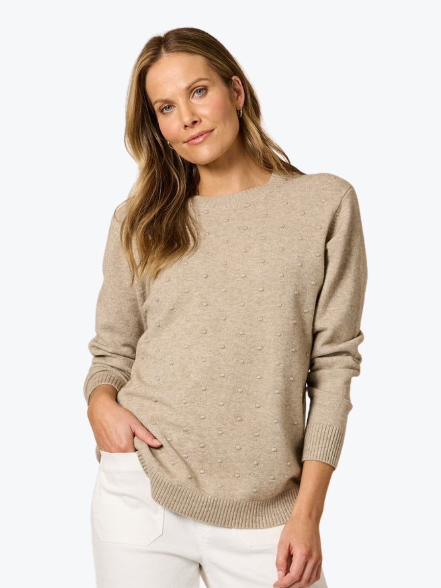 Woman wearing a beige sweater and white pants on a white background