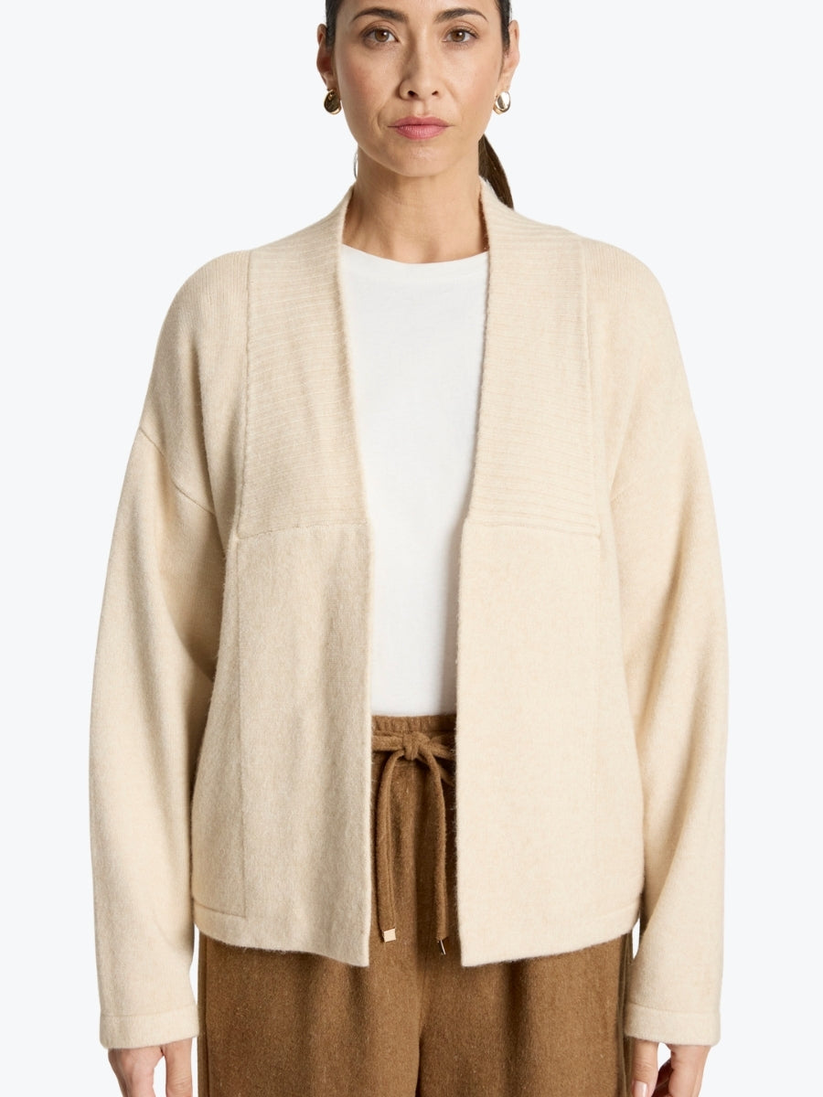 Woman wearing a beige cardigan over a white shirt and brown pants on a white background