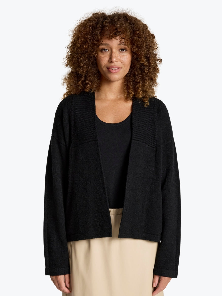 Woman wearing a black cardigan over a black top with beige pants on a white background