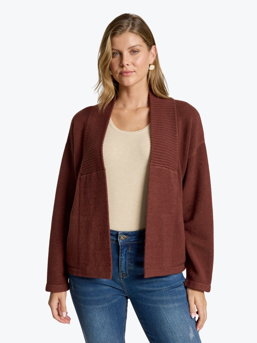 Woman wearing a brown cardigan over a beige top and blue jeans on a white background