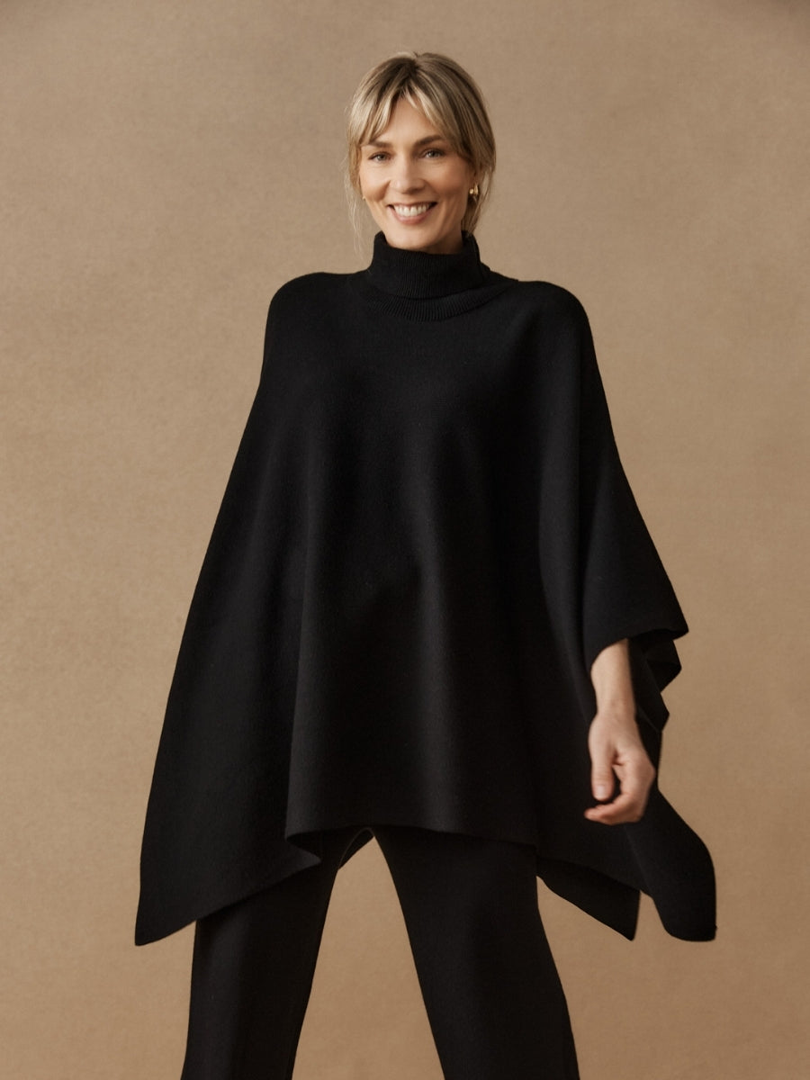 Woman wearing a black poncho against a beige background