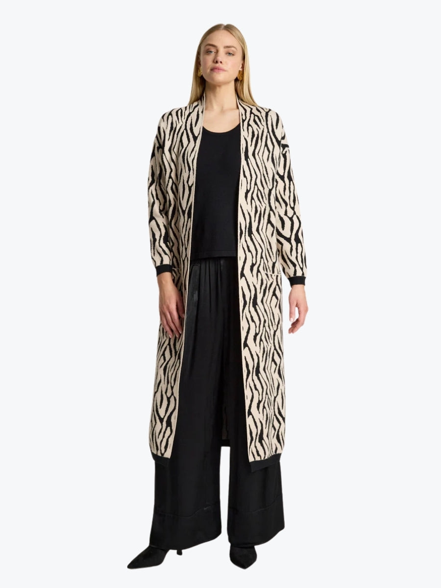Woman wearing a long zebra print coat over black attire on a white background