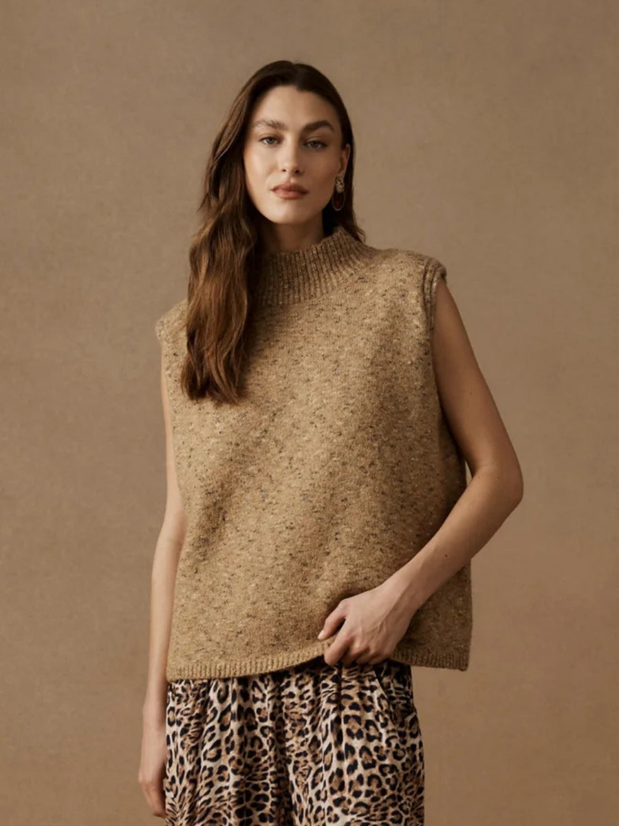 Woman wearing a beige knitted vest against a brown background