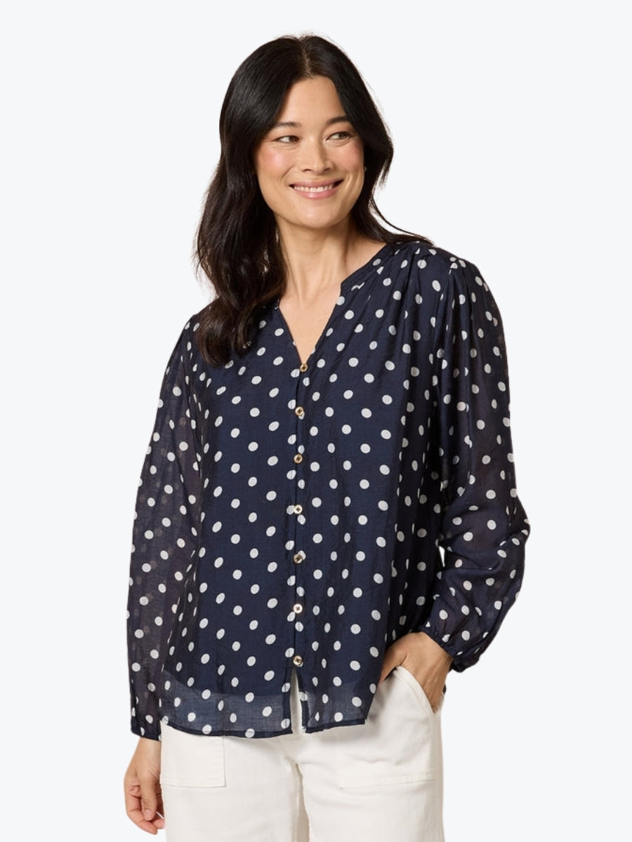 Woman wearing a navy blue blouse with white polka dots on a white background