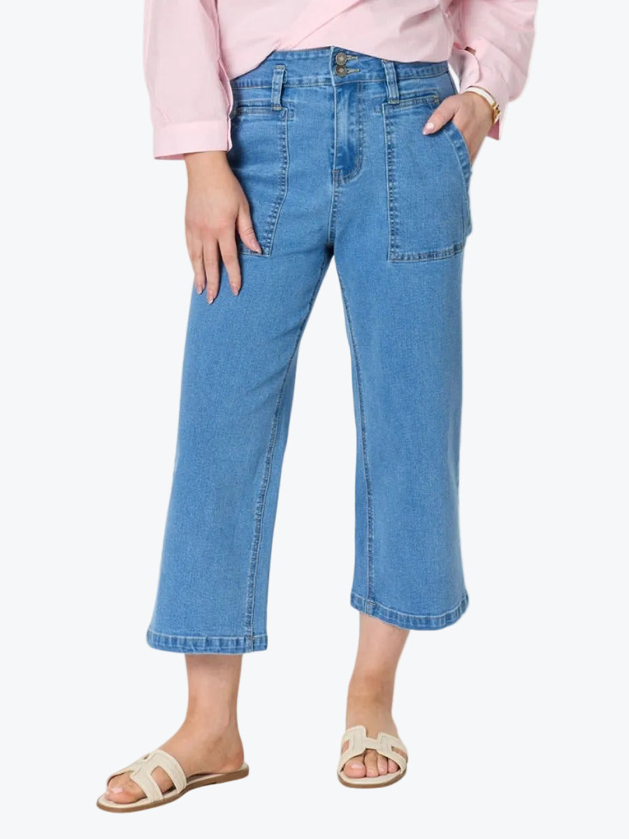 A model wearing light blue cropped denim jeans with a pink shirt and beige slide sandals, shown from the waist down on a white background.