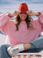 Person wearing a pink sweater and red beanie with mountains in the background