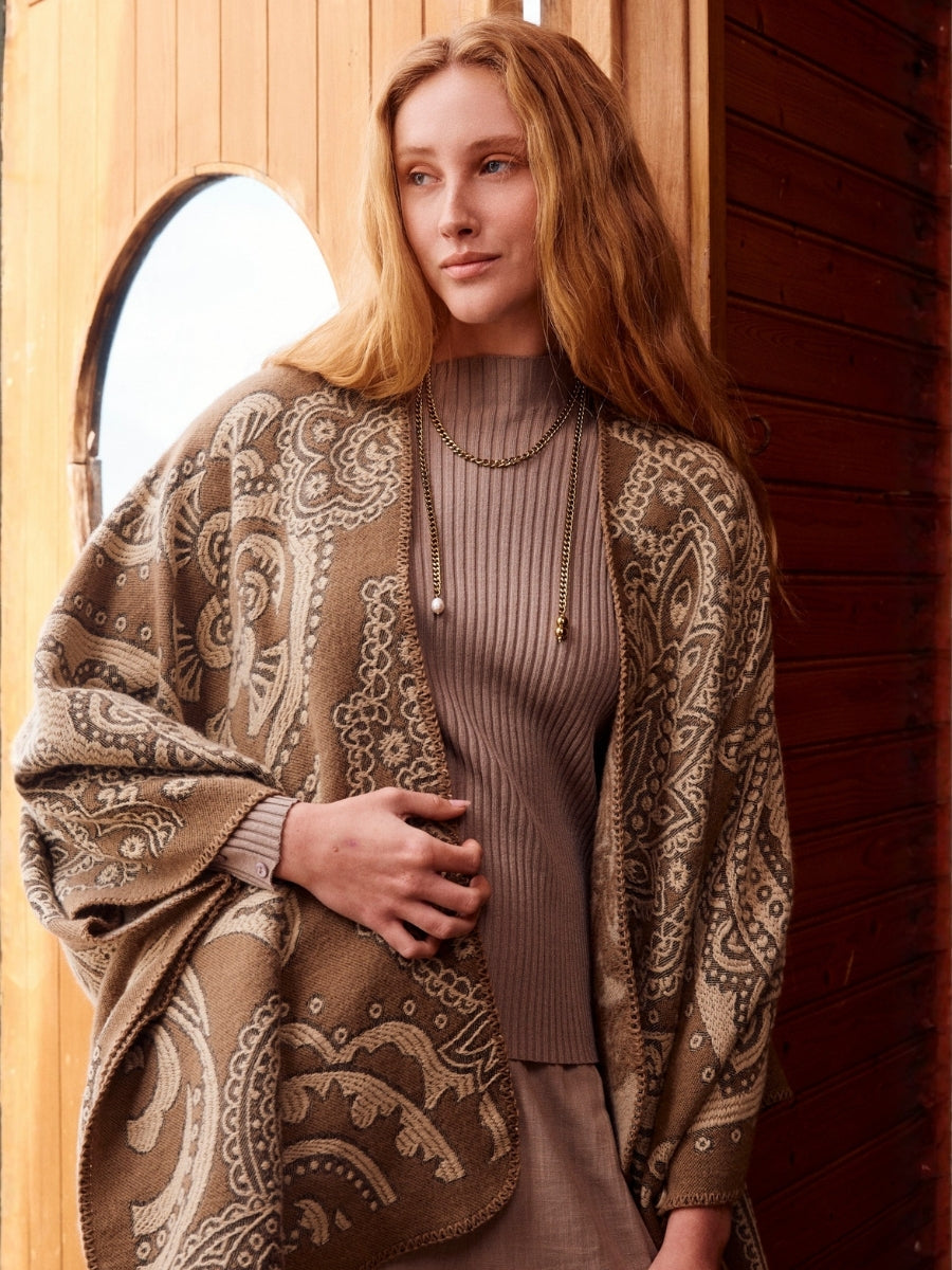 Woman wearing a patterned cardigan in front of a wooden door.