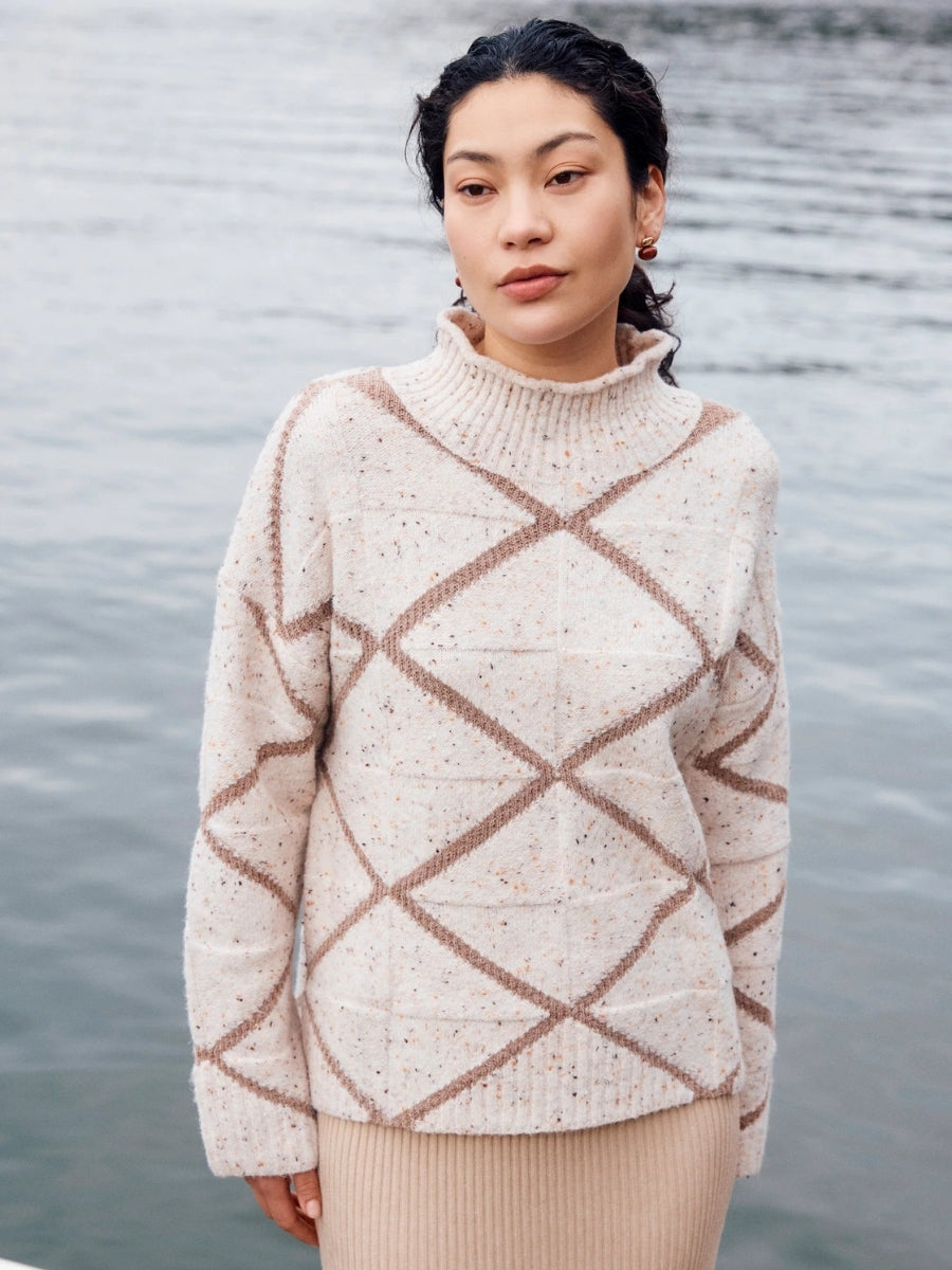 Person wearing a patterned sweater standing by a body of water