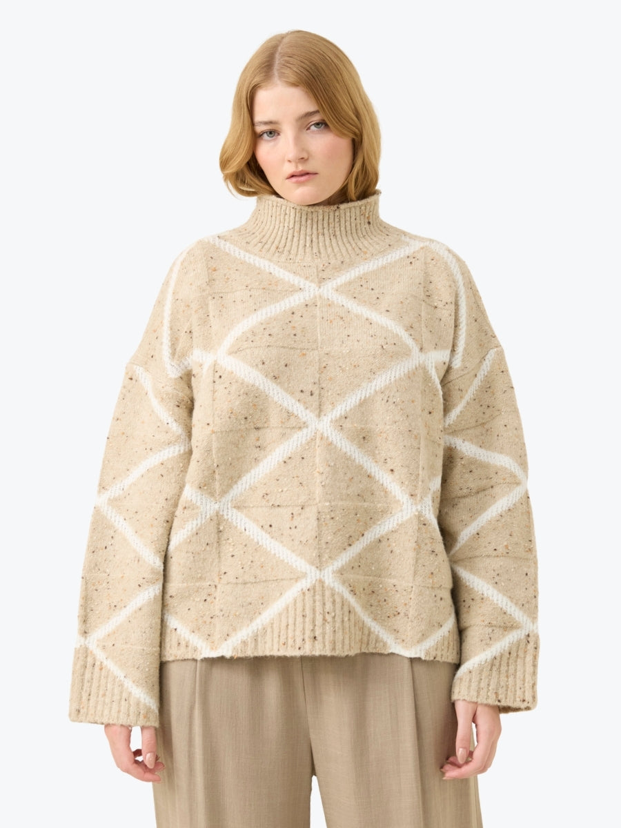 Woman wearing a beige sweater with white geometric patterns on a white background