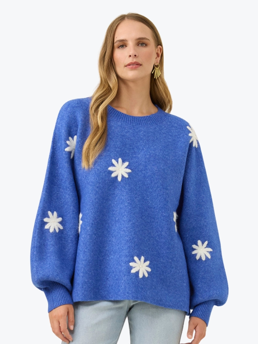 Woman wearing a blue sweater with white floral patterns on a light gray background