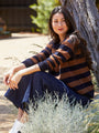 Woman sitting outdoors wearing a striped sweater and dark pants.
