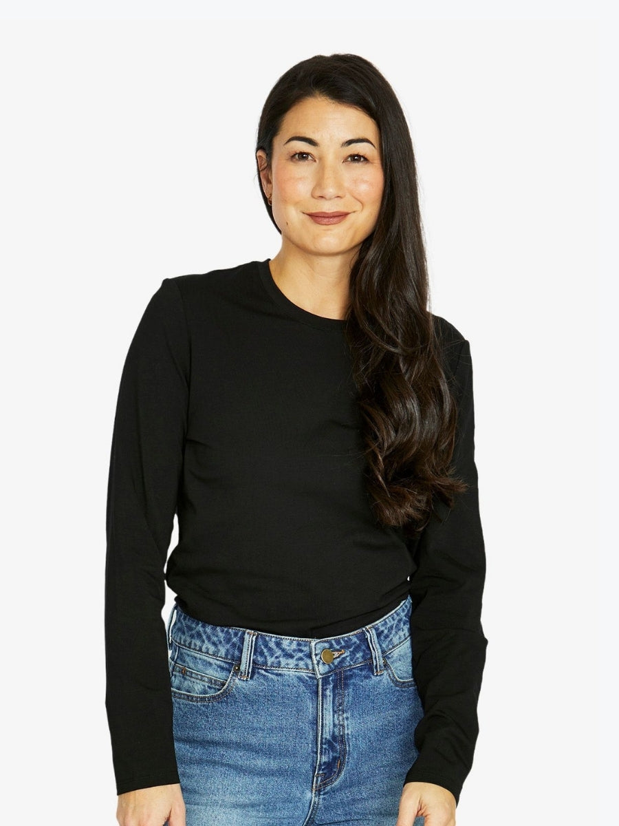 Woman wearing a black long-sleeve top and blue jeans on a white background