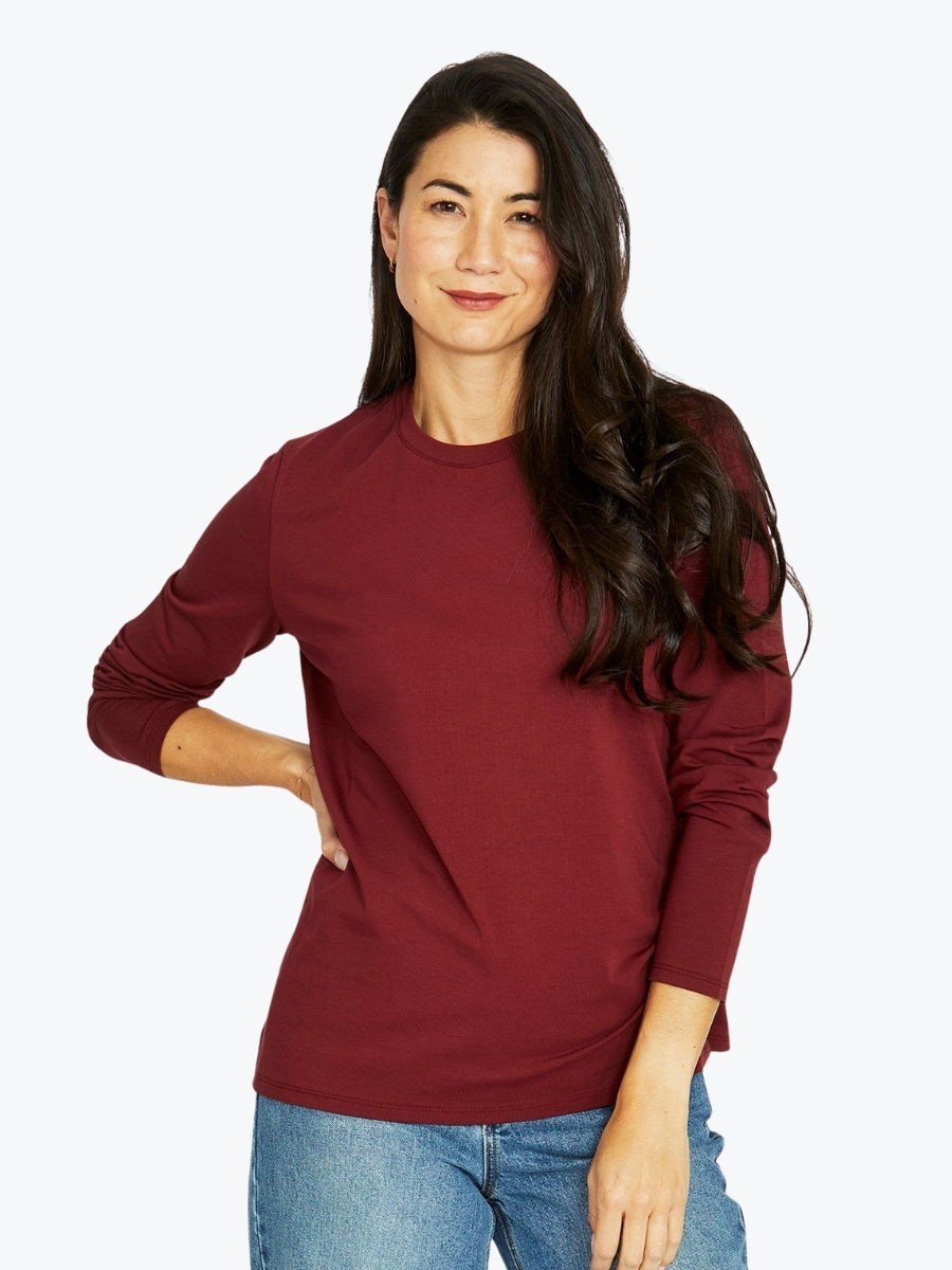 Woman wearing a maroon long-sleeve shirt and blue jeans on a white background