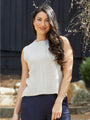Woman wearing a white sleeveless sweater and dark pants standing outdoors.