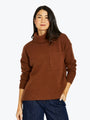 Woman wearing a brown turtleneck sweater with a pocket on a white background