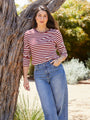 Woman wearing a red and white striped shirt and blue jeans standing next to a tree