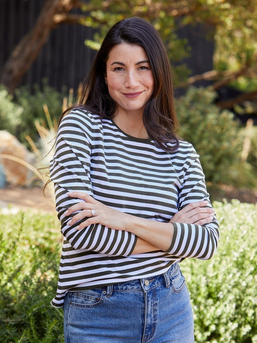 Woman wearing a striped shirt and jeans standing outdoors with greenery in the background