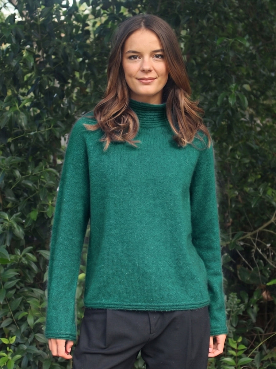 Woman wearing a green sweater standing in front of green foliage