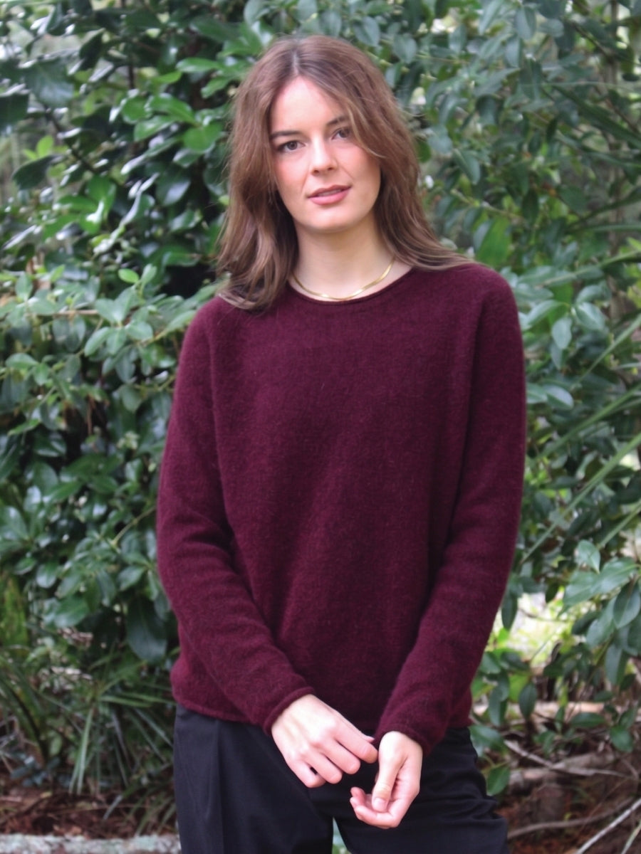 Woman wearing a burgundy sweater standing in front of green foliage