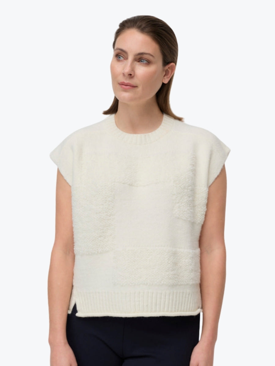 Woman wearing a white sleeveless knitted top against a white background