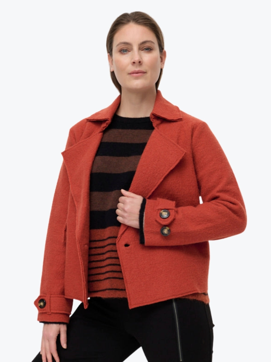 Woman wearing a red coat over a striped sweater on a white background