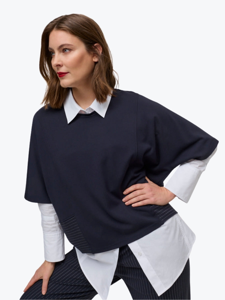 Woman wearing a navy sweater over a white shirt with a plain background