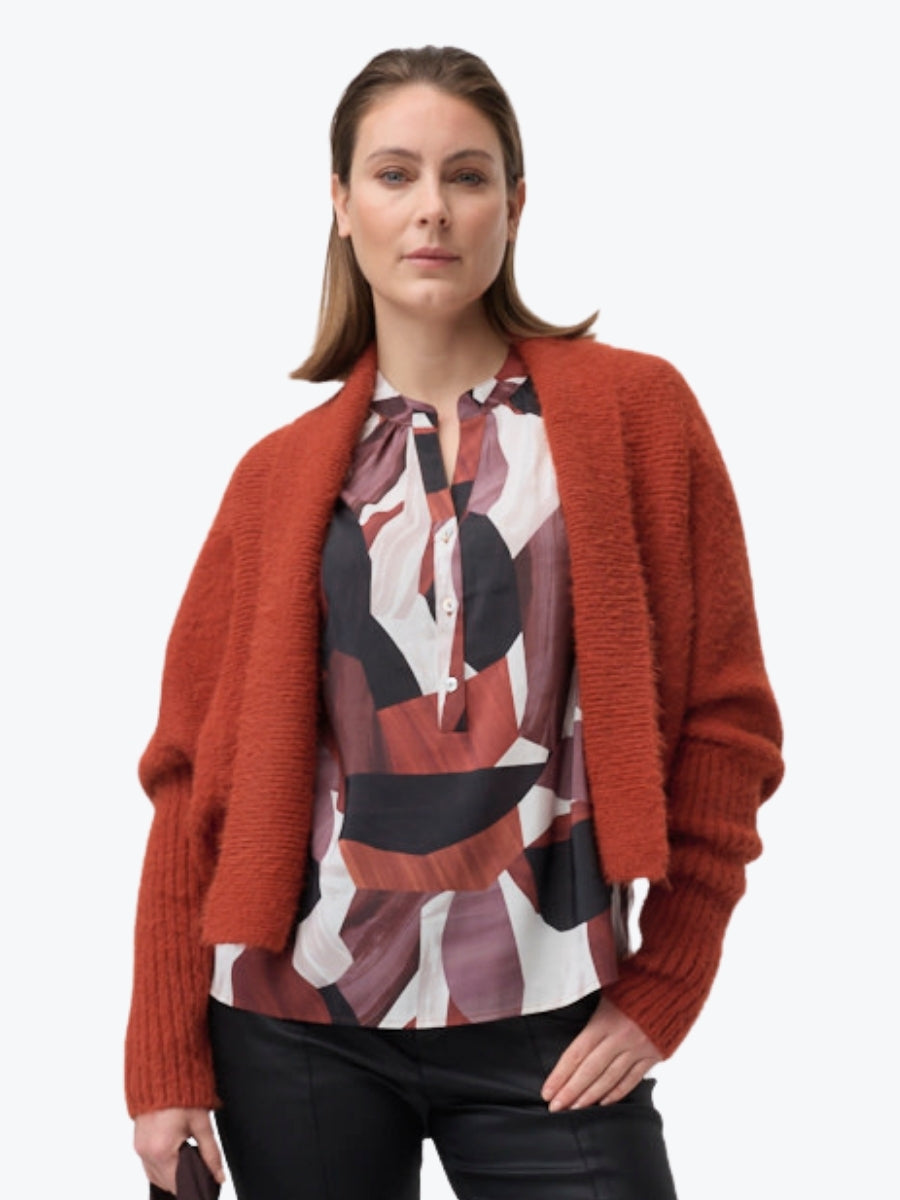 Woman wearing a rust-colored cardigan over a patterned blouse on a white background