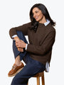 Woman sitting on a stool wearing a brown sweater, blue pants, and brown shoes.