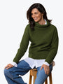 Woman wearing a green sweater over a white shirt and blue jeans on a white background