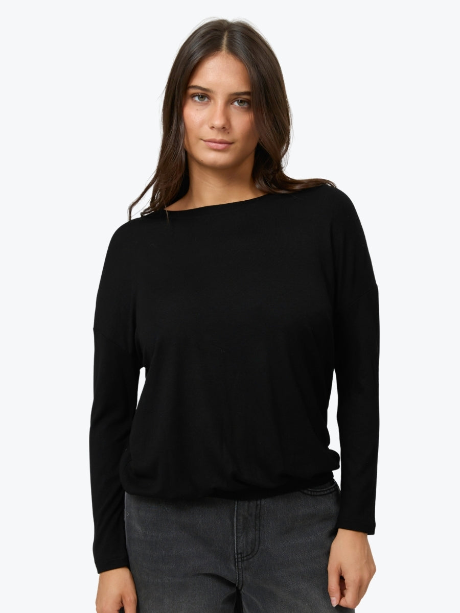 A woman modeling a black long-sleeve boat-neck top with dark gray jeans against a plain white studio background.