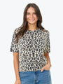A woman wearing a short-sleeve crewneck top with a beige, black, and brown leopard print pattern, paired with blue jeans, against a plain light gray background.