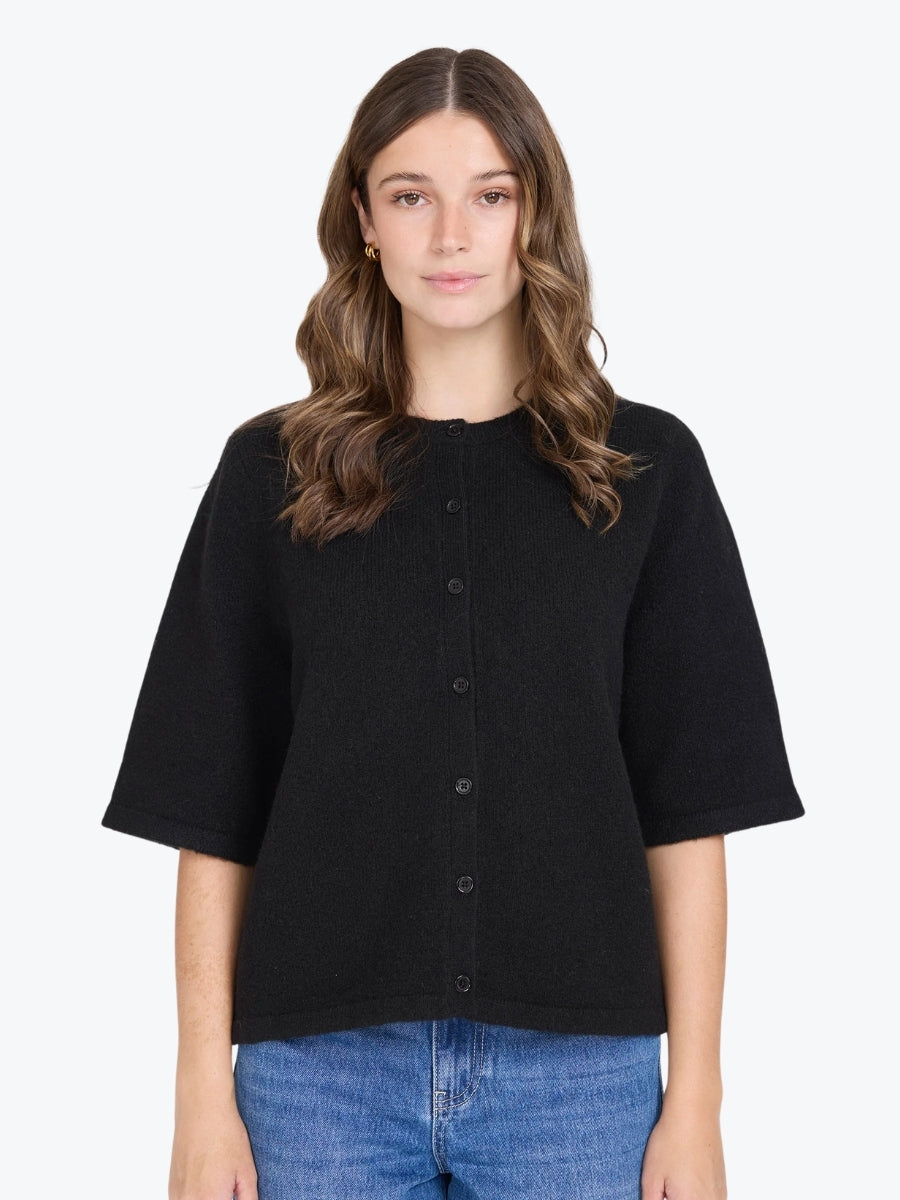 Woman wearing a black short-sleeve button-up shirt and blue jeans on a white background