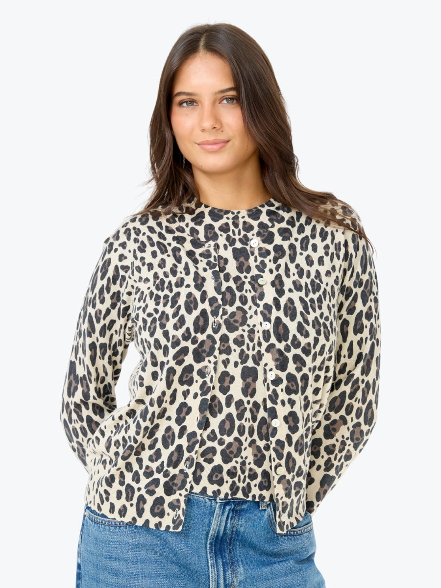 A woman wearing a beige and black leopard print long-sleeve top with blue jeans, photographed against a plain light gray background.