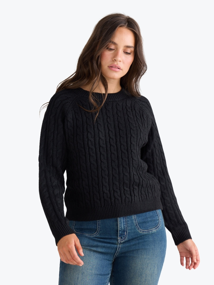 Woman wearing a black cable knit sweater and blue jeans on a white background
