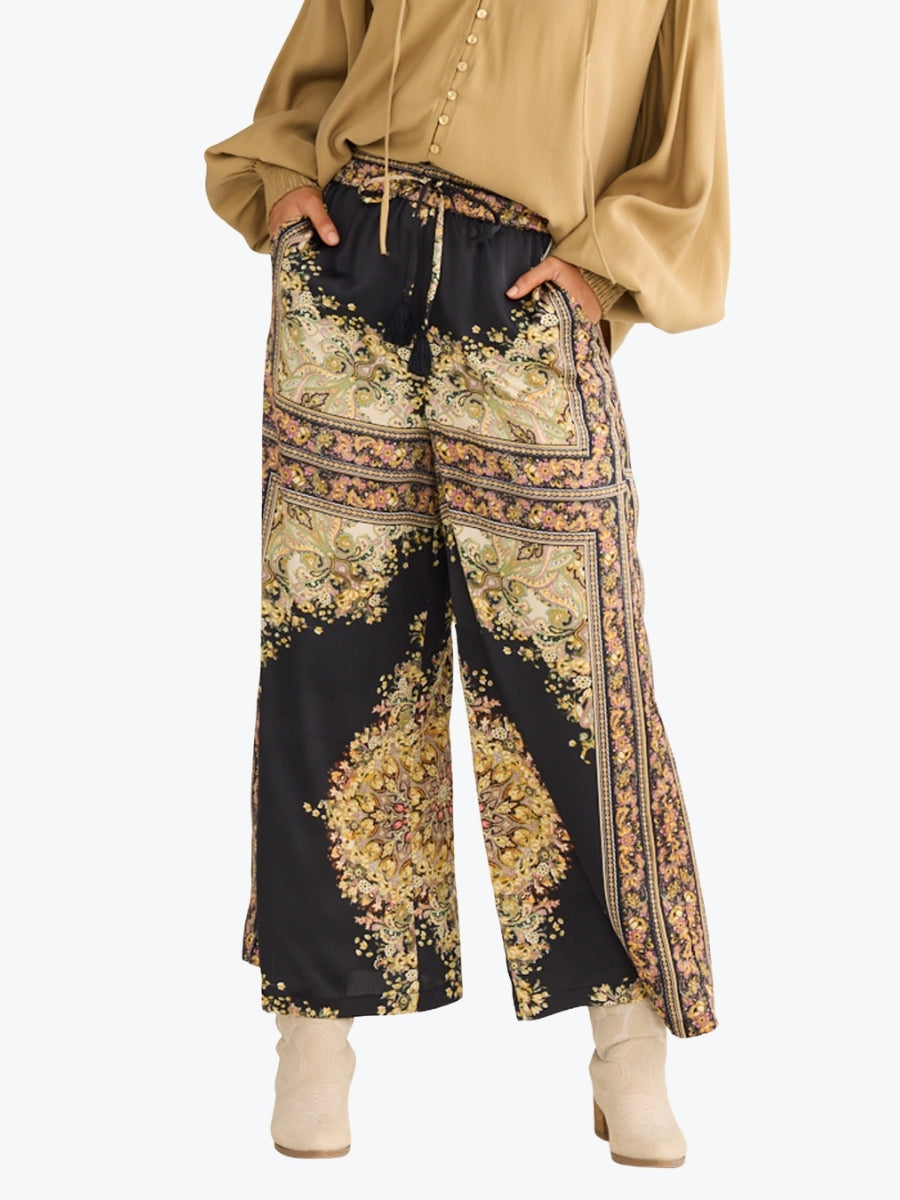 Person wearing a beige top and black floral patterned pants on a white background
