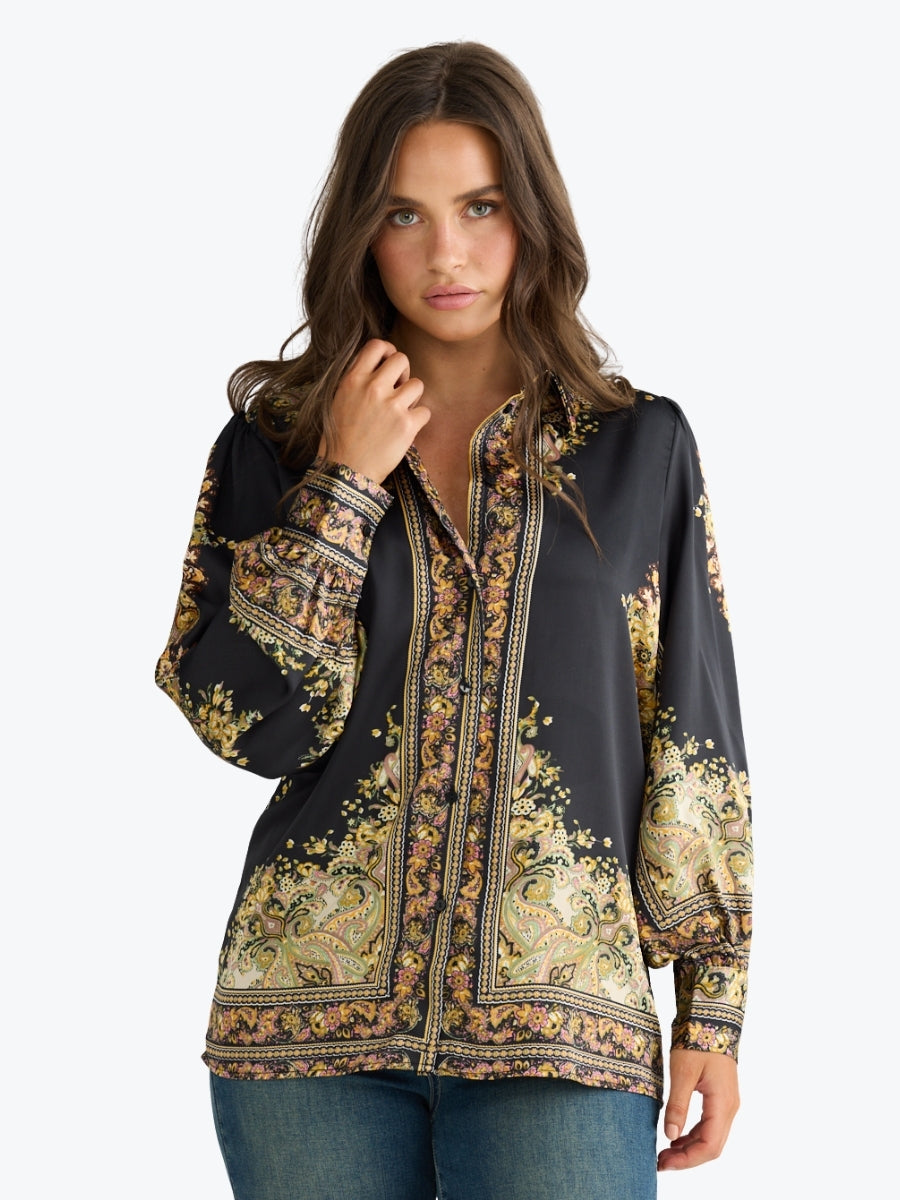 Woman wearing a black blouse with intricate gold and beige patterns on a white background