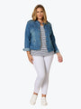 Woman wearing a denim jacket, striped shirt, and white pants on a white background