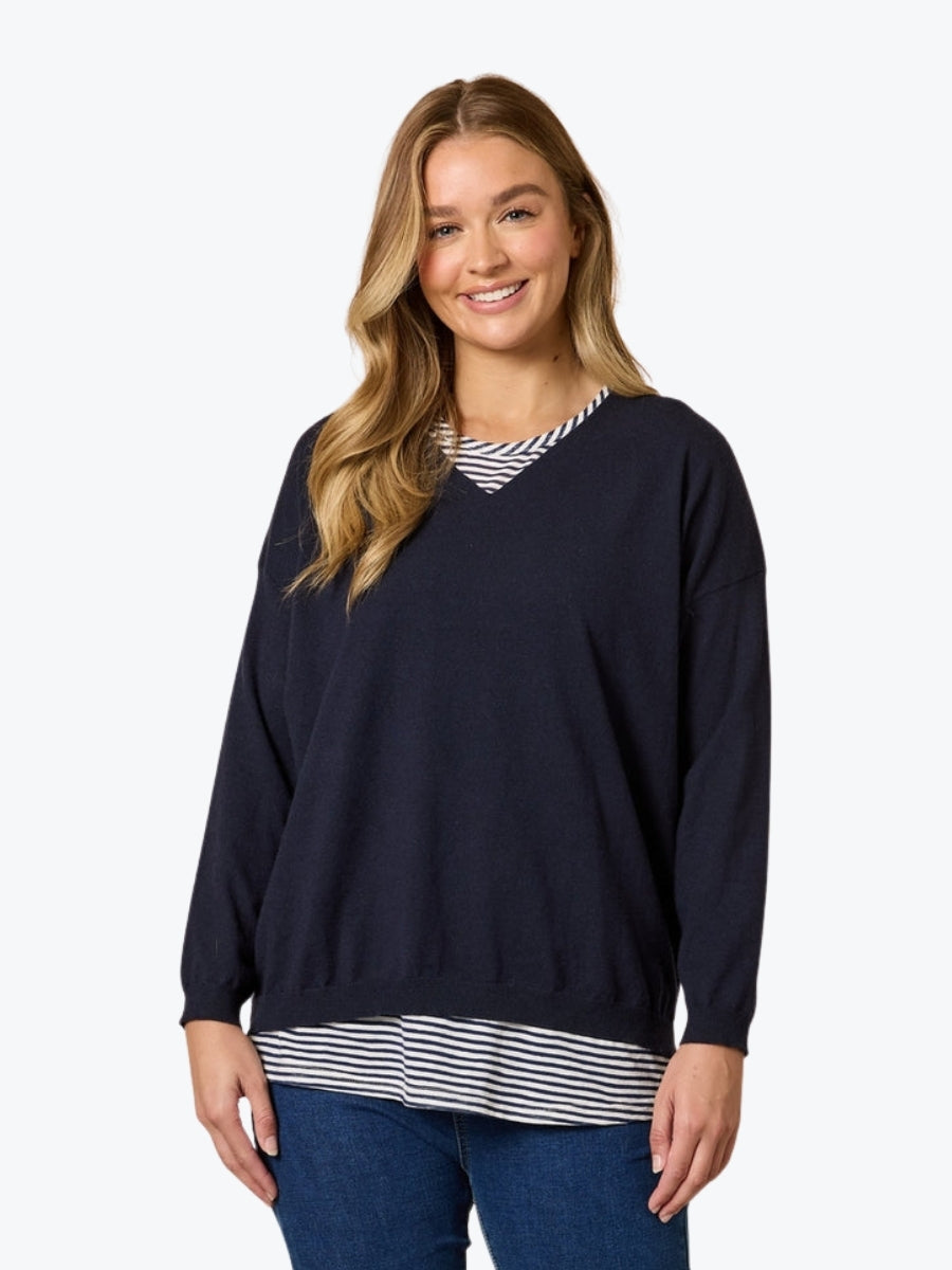 Woman wearing a navy sweater over a striped shirt on a white background