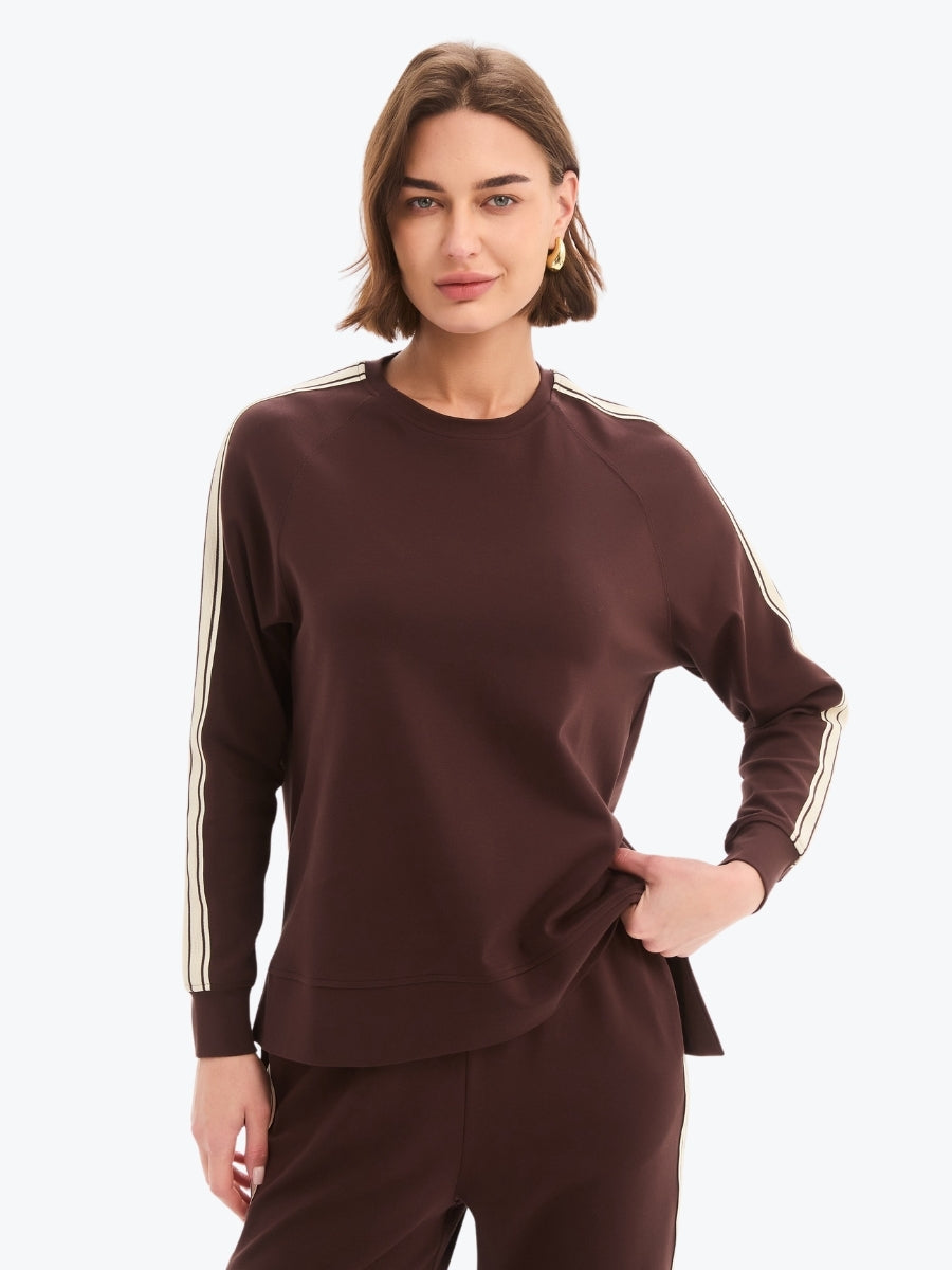 Woman wearing a brown sweatshirt with white stripes on sleeves against a white background
