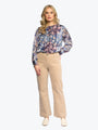 Woman wearing a floral blouse and beige pants on a white background