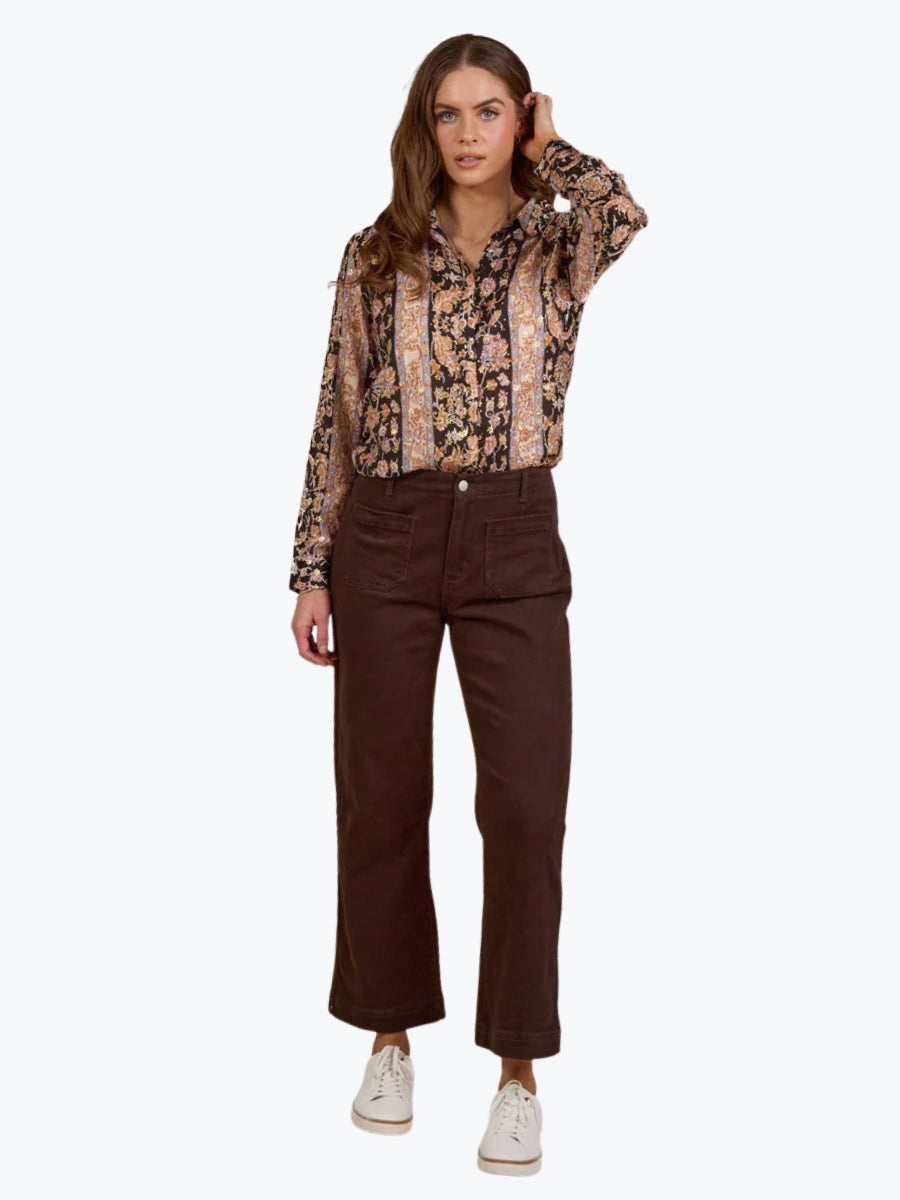 Woman wearing a patterned blouse and brown pants on a white background