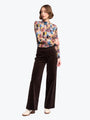 Woman wearing a colorful patterned shirt and brown pants on a white background