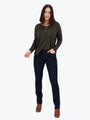 Woman wearing a dark green long-sleeve top and black jeans on a white background